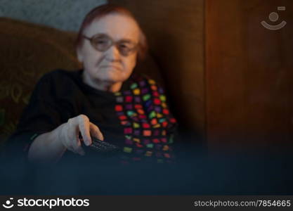 View from behind the television set of an elderly lady watching television using the remote to change channels
