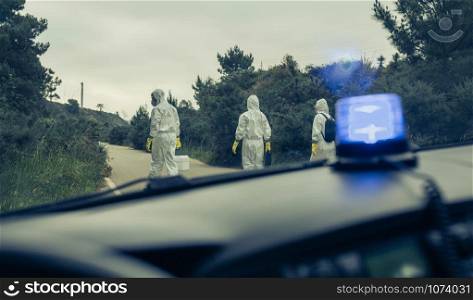 View from emergency car of people with bacteriological protection suits walking on a road looking for evidence. View from emergency car of people with bacteriological protection suits