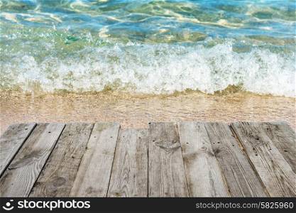 View from empty wooden deck table to tropical sunny beach with surf and blue water background