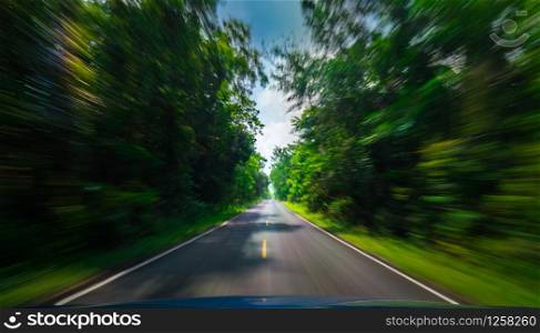 View from front of blue car on asphalt road and speed motion blur on highway in summer with green trees forest at countryside