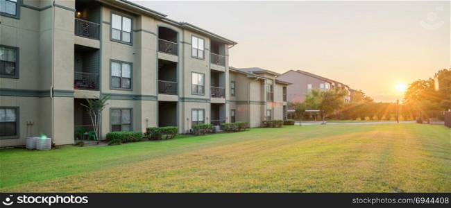 View from grassy backyard of a typical apartment complex building in suburban area at Humble, Texas, US. Sunset with warm light. Panorama style.