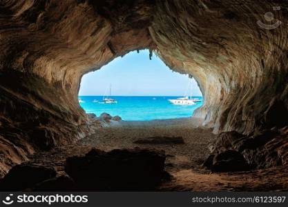 View from inside of big cave to the beach and blue sea. Mediterranean coast, Sardinia, Italy.