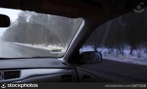 View from inside of car on winter landscape. Woman driving automobile on freeway during snow through the forest in wintertime.