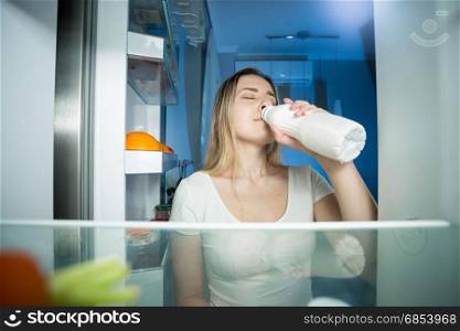 View from inside of refrigerator on young woman drinking milk at night