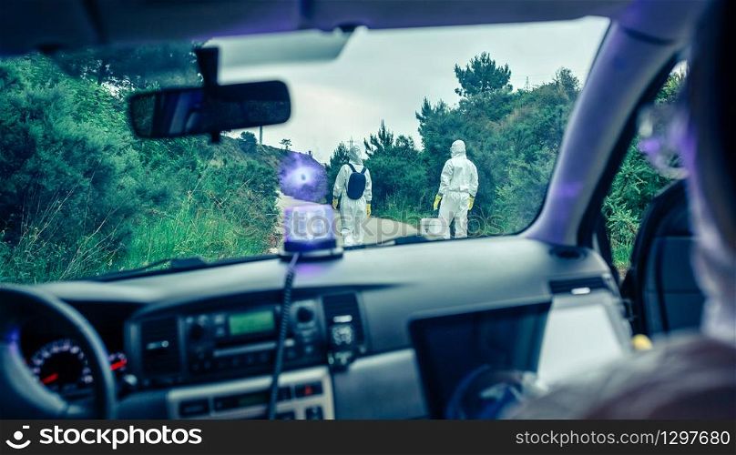 View from inside the car of people in bacteriological protection suits doing research on an empty road