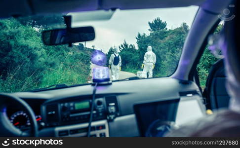 View from inside the car of people in bacteriological protection suits doing research on an empty road