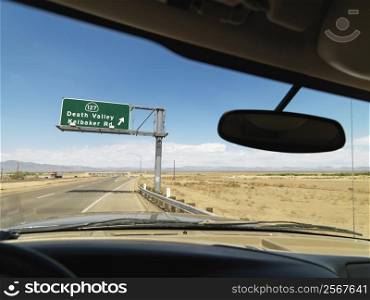 View from inside vehicle on desert highway with sign pointing towards Death Valley.