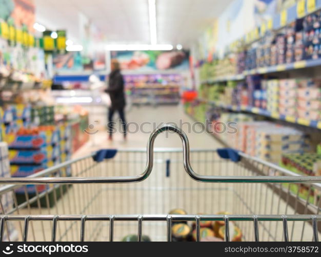 View from shopping cart trolley basket at supermarket self-service grocery shop. Retail. Blurred background.