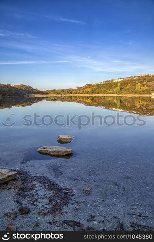 View from shore with fall foliage colors reflected in still lake water on a beautiful autumn day