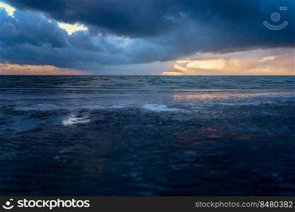 View from the beach on the wadden sea with dramatic storm clouds which sun rays shine  through. Cloudy sky with sunbeams above the coast