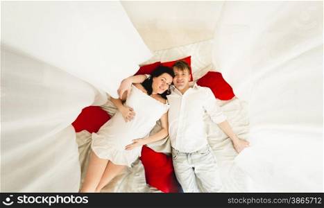 View from top of happy husband hugging pregnant wife on big bed with baldachin