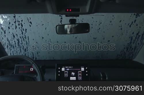 View inside car of automatic car wash brushes in action during washing process at service station. Automatic car wash brushes cleaning soap