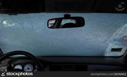 View inside of car. Young female driver cleaning car windshield from snow with the help of blue snow brush.