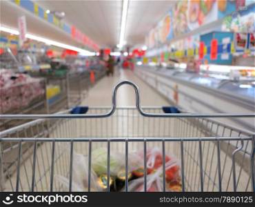 view of a shopping cart with grocery items at supermarket blurred background