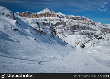 View of a ski resort piste with people skiing in Dolomites in Italy. Ski area Arabba. Arabba, Italy. Ski resort in Dolomites, Italy