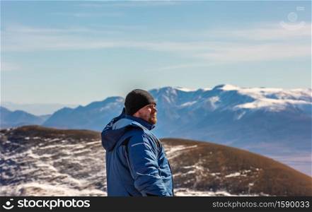 View of a tourist looking in the distance in the mountains. White snowy mountain ridge and beautiful blue cloudy sky as a background and slightly out of focus. Altai mountains, Siberia, Russia.. View of a tourist looking in the distance in the mountains. White snowy mountain ridge and beautiful blue cloudy sky as a background and slightly out of focus. Altai mountains, Siberia, Russia