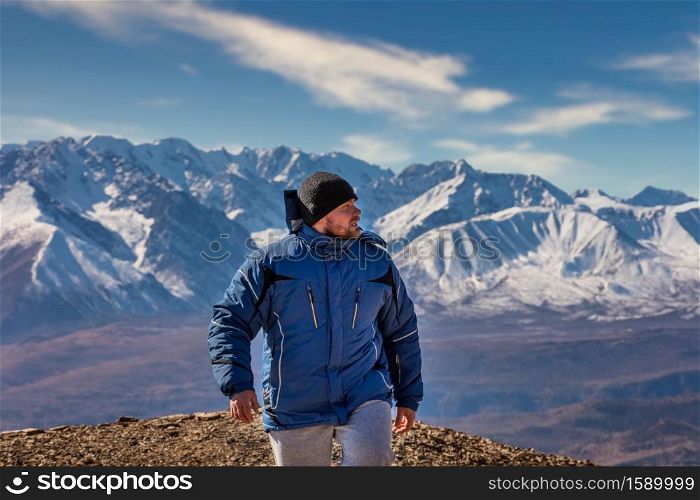 View of a tourist walking in the mountains. White snowy mountain ridge and beautiful blue cloudy sky as a background and slightly out of focus. Altai mountains, Siberia, Russia.. View of a tourist walking in the mountains. White snowy mountain ridge and beautiful blue cloudy sky as a background and slightly out of focus. Altai mountains, Siberia, Russia