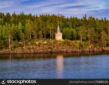 View of a wooden church standing on a rocky shore surrounded by forest. Chapel by the river among the trees