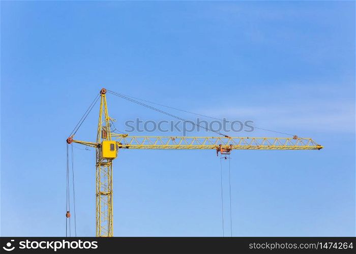 View of a yellow crane. Blue sky background. Long jib-arm. Construction site.