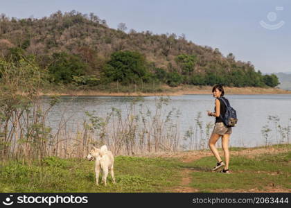 View of a young asia woman with white dog enjoying peaceful moment of beautiful view lake shore with mountains range in background. Pet and woman, Rest and enjoyment, lifestyle, Selective focus.