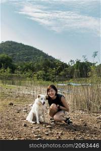 View of a young asia woman with white dog enjoying peaceful moment of beautiful view lake shore with mountains range in background. Pet and woman, Rest and enjoyment, lifestyle, No focus, specifically.