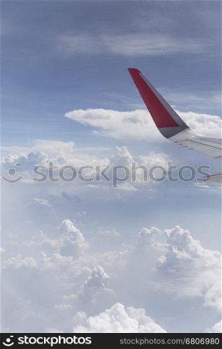 view of airplane wing and cloudscape in blue sky from aircraft window