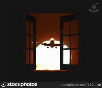 View of an aeroplane gliding towards a window frames with the sun behind it