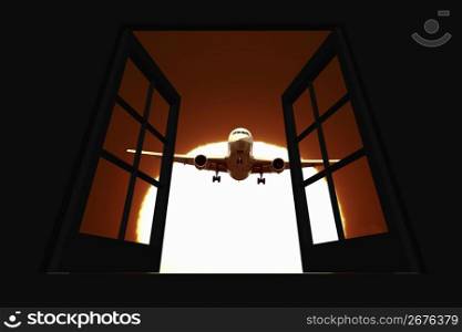 View of an aeroplane gliding towards a window frames with the sun behind it