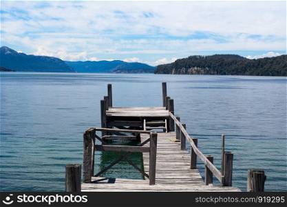 View of an empty wooden pier on lake with blue sky on background.