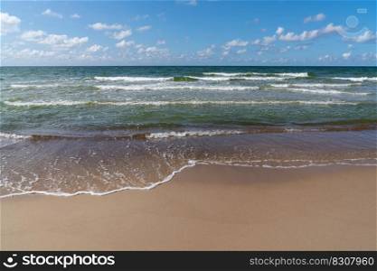 View of an idyllic sandy beach with gentle waves lapping at the shore under a blue summer sky with white clouds and coyp space