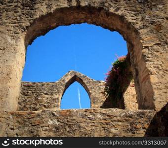 View of an old arch in San Juan Mission in Texas with modern jet trail in sky