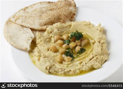 View of Arab masbacha, hummus dip served with whole chickpeas and a chilli and lemon flavoured sauce and unleavened pita bread.
