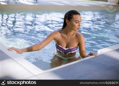 View of attractive young woman in bikini standing on the poolside of outdoor swimming pool at summer