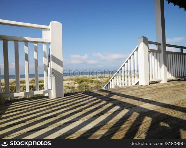 View of beach from porch with railing casting shadow on wooden deck at Bald Head Island, North Carolina