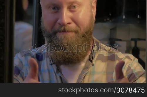 View of bearded bald man in checkered shirt smiling and showing thumbs up