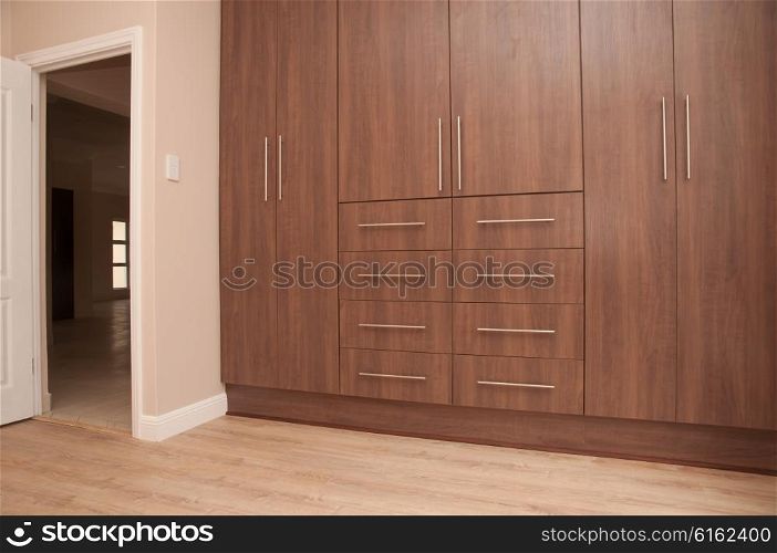 View of dark brown build in wooden cupboards of an empty bedroom in a newly build house. Next to the cupboards is the entrance to the bedroom and the floor is of laminated wood.