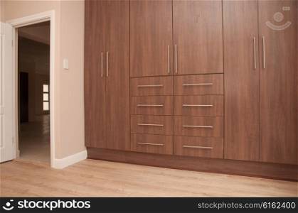 View of dark brown build in wooden cupboards of an empty bedroom in a newly build house. Next to the cupboards is the entrance to the bedroom and the floor is of laminated wood.