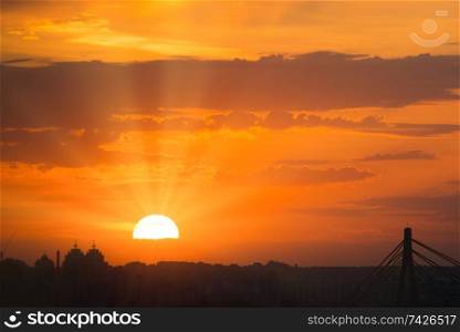 View of dramatic sunset with orange sky, bright sun and dark silhouette of city buildings at skyline