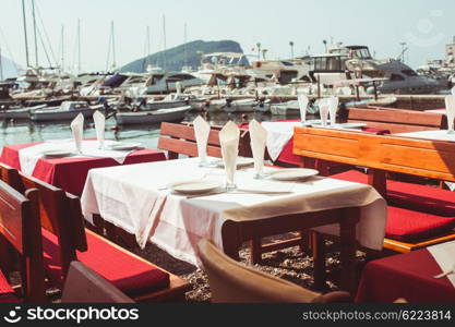 View of empty outdoor cafe near lagoon with yachts. Classic table setting