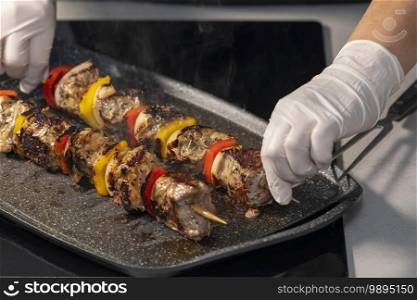 view of female chef using gloves picking up a smoking beef skewer from a roasting tray. Selective focus and close up.. Female using gloves picking up a smoking beef skewer from a roasting tray