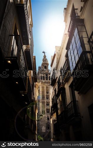 View of Giralda tower of Cathedral of Saint Mary of the See, Seville Cathedral, through a narrow street, Andalucia, Spain.. View of Giralda tower of Cathedral of Saint Mary of the See, Seville Cathedral, through a narrow street, Andalucia, Spain
