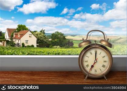 View of house on summer vineyard landscape from window with alarm clock