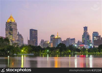 View of lake in Lumpini park with high building of business center district of Bangkok in background at sunset. Travel to Thailand.