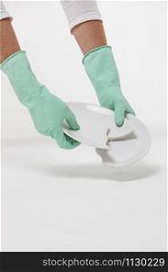 View of man hands in protective rubber gloves picking up a broken plate from the floor during cleaning or after a quarrel. Isolated on white background. Cleanup concept.