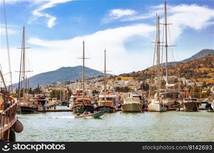 View of many yachts and boats moored at Bodrum harbor in a sunny summer day. Cloudy sky and mountains on the background.. View of many yachts and boats moored at Bodrum harbor in a sunny summer day.