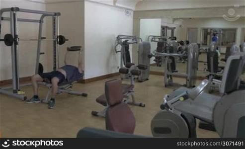 View of modern gymnasium. Man exercising with weight disk and another person working on pull down machine in mirror reflection