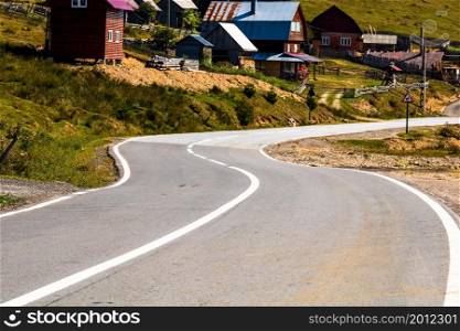 View of mountain road thorugh houses and trees in Bihor, Romania, 2021