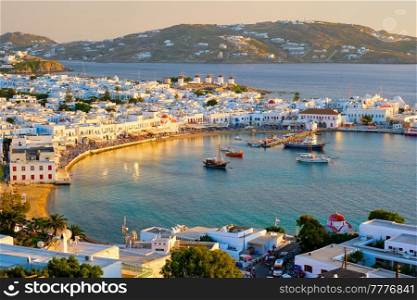 View of Mykonos town Greek tourist holiday vacation destination with famous windmills, and port with boats and yachtson sunset . Mykonos, Cyclades islands, Greece. Mykonos island port with boats, Cyclades islands, Greece