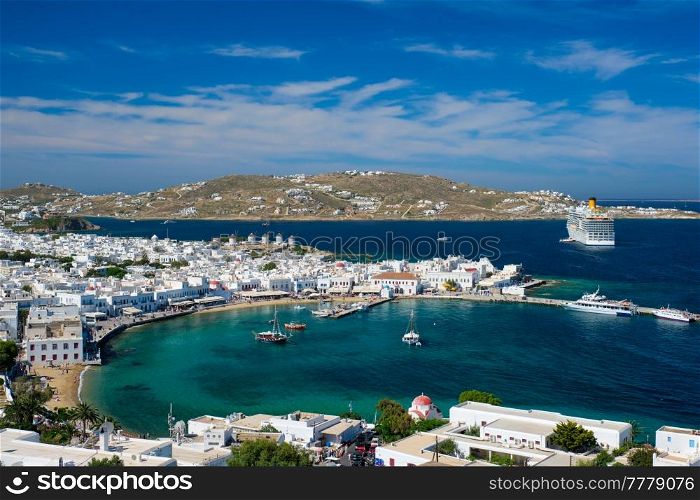 View of Mykonos town Greek tourist holiday vacation destination with famous windmills, and port with boats and yachts and cruise liner. Mykonos, Cyclades islands, Greece. Mykonos island port with boats, Cyclades islands, Greece