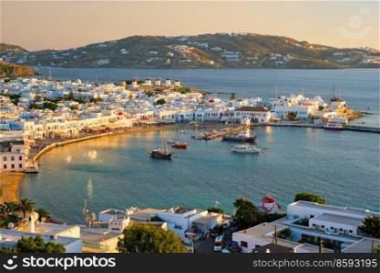 View of Mykonos town Greek tourist holiday vacation destination with famous windmills, and port with boats and yachtson sunset . Mykonos, Cyclades islands, Greece. With horizontal camera panning. Mykonos island port with boats, Cyclades islands, Greece